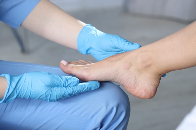 A doctor in blue gloves examining a patient's foot in a hospital setting.