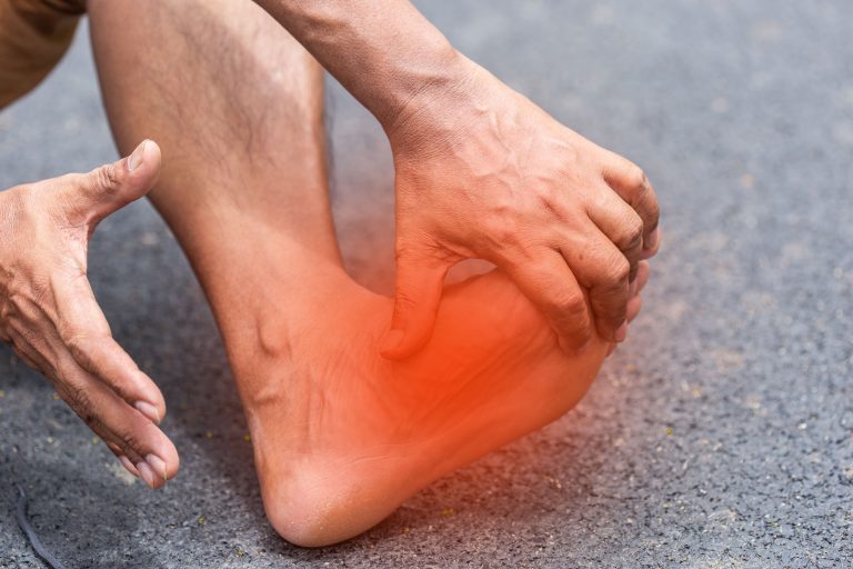 A close-up image of a man's ankle showing symptoms of pain as he holds it.