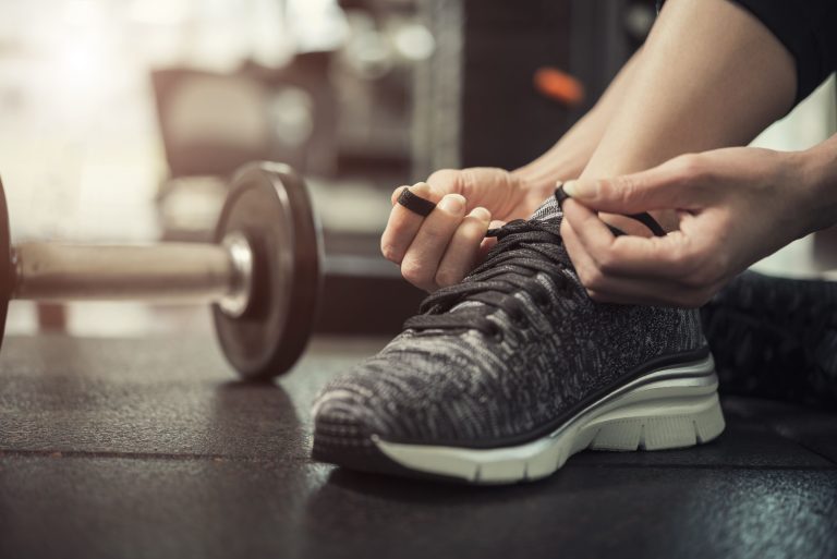 A close-up of a woman tying her running shoes in a gym setting, ready for a workout.