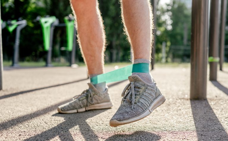 A person training outdoors with a resistance band around their ankles, wearing athletic shoes.