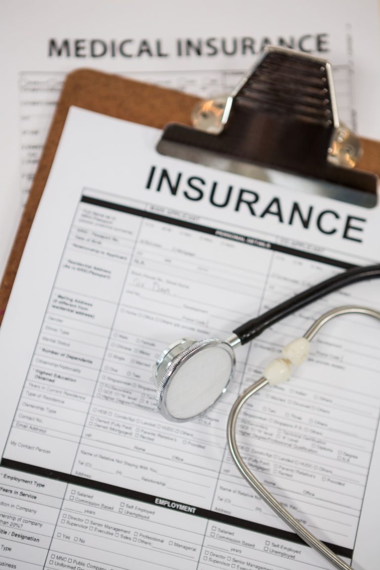 A medical insurance form is placed on a clipboard alongside a silver stethoscope.