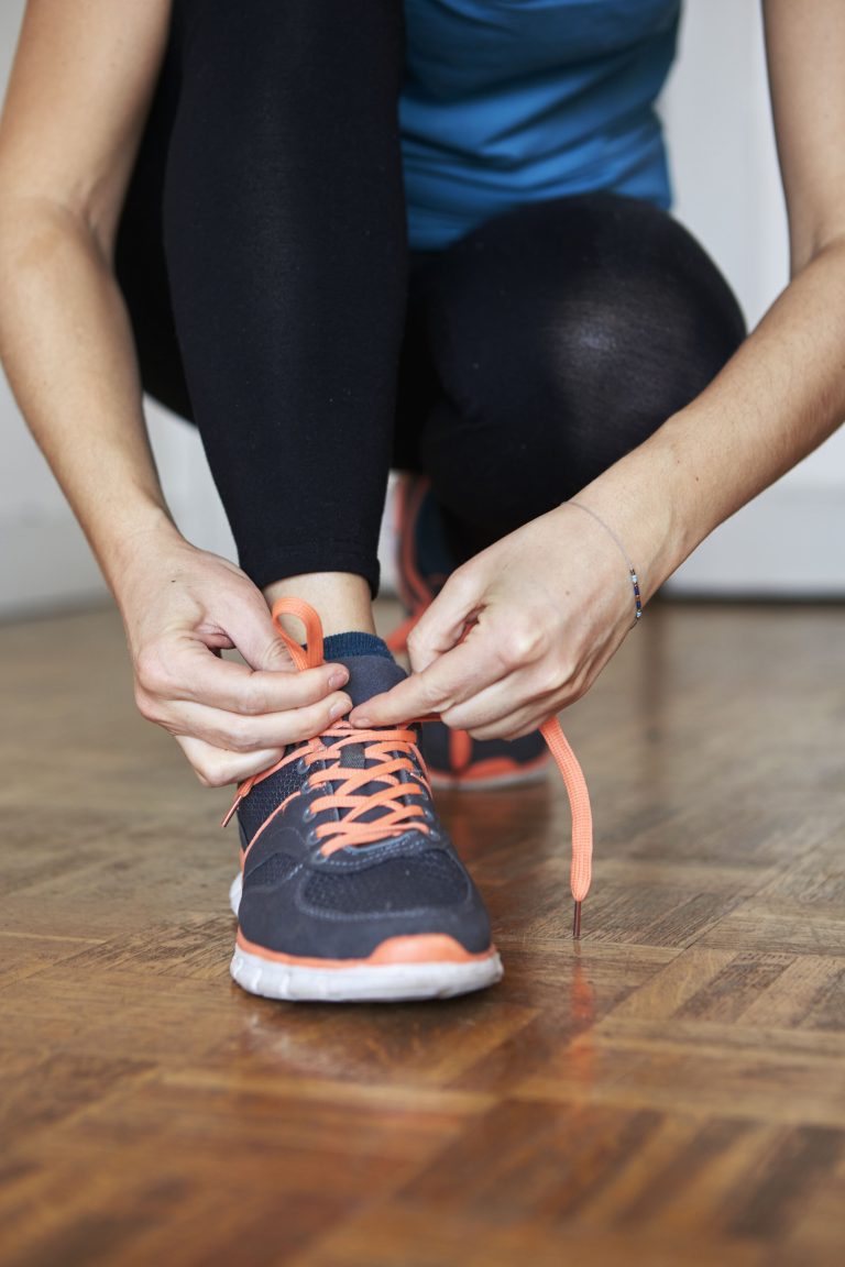 A woman tying her shoelaces before starting a workout in her home.